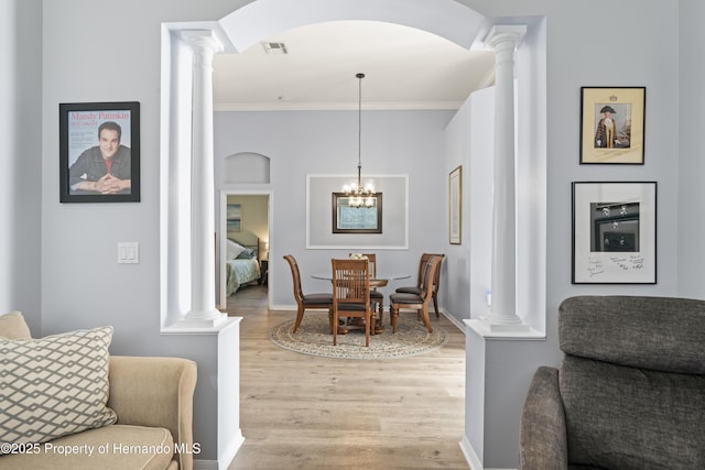 dining area featuring visible vents, a notable chandelier, light wood-style floors, crown molding, and decorative columns