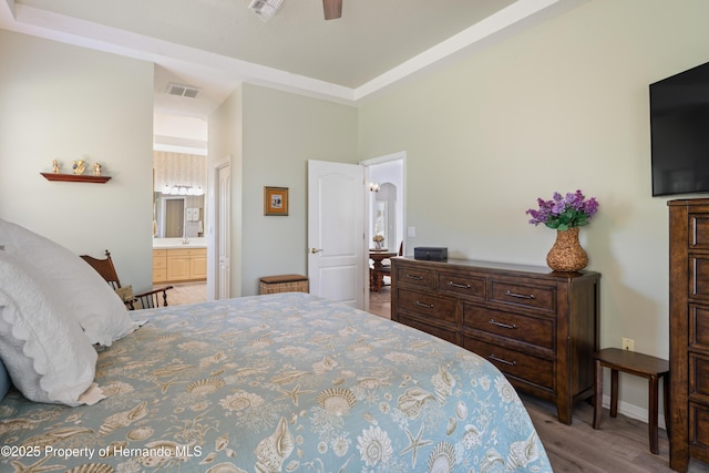 bedroom with ensuite bath, wood finished floors, visible vents, and ceiling fan