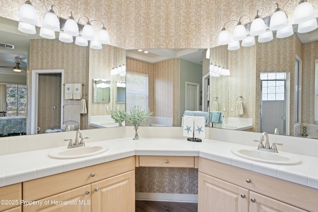 bathroom featuring wallpapered walls, double vanity, a shower stall, and a sink