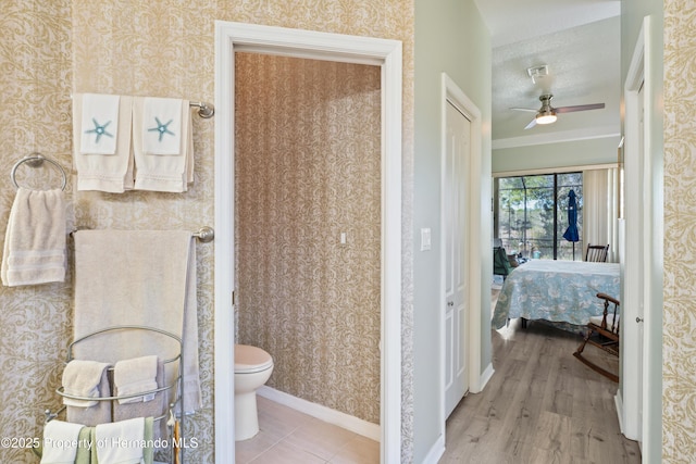 bathroom with toilet, wallpapered walls, baseboards, and a ceiling fan