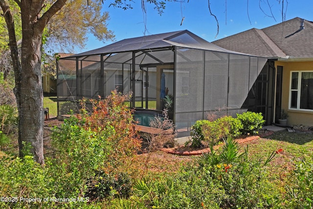 exterior space with a lanai, a lawn, a shingled roof, and stucco siding