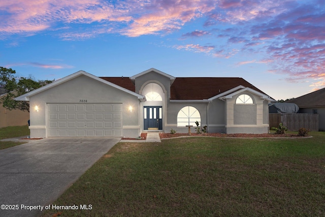 single story home with a garage, a lawn, driveway, and stucco siding