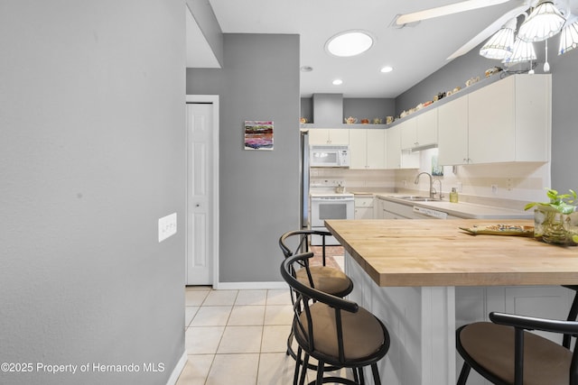 kitchen featuring a breakfast bar area, white appliances, wood counters, a sink, and white cabinetry