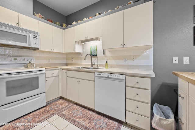 kitchen featuring a textured wall, white appliances, a sink, light countertops, and tasteful backsplash