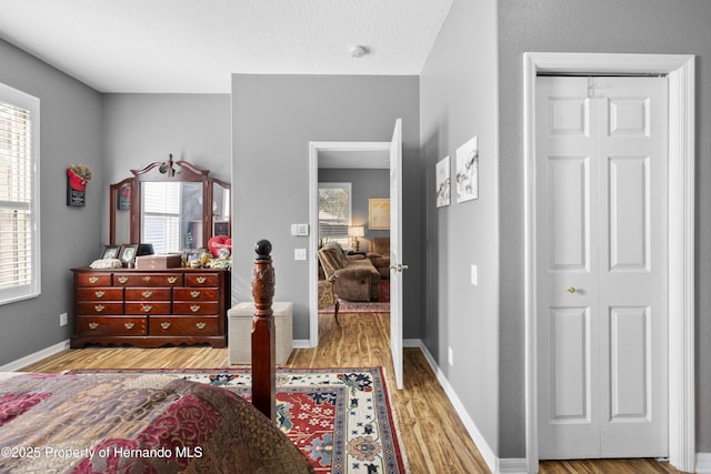 bedroom featuring a textured ceiling, multiple windows, light wood-type flooring, and baseboards