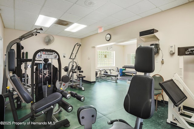 exercise room featuring a paneled ceiling and baseboards