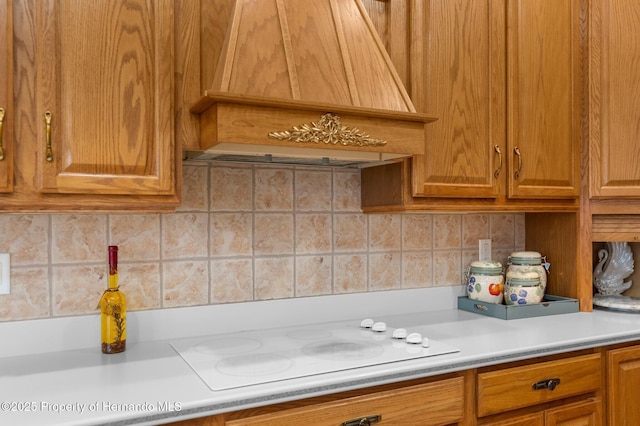 kitchen featuring white electric stovetop, brown cabinets, backsplash, light countertops, and custom range hood