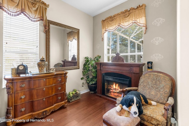 living area featuring baseboards, a glass covered fireplace, and wood finished floors