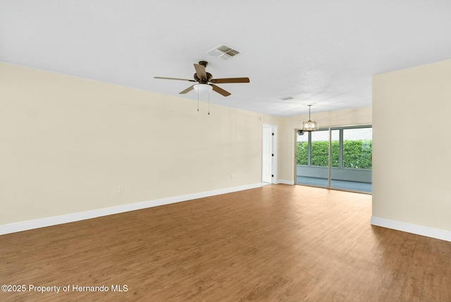 unfurnished room featuring baseboards, visible vents, wood finished floors, and ceiling fan with notable chandelier