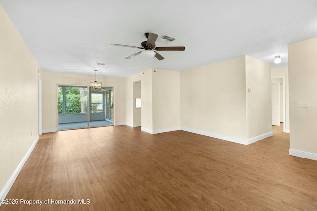 spare room featuring ceiling fan with notable chandelier, visible vents, baseboards, and wood finished floors