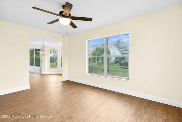 spare room featuring baseboards, wood finished floors, and ceiling fan with notable chandelier