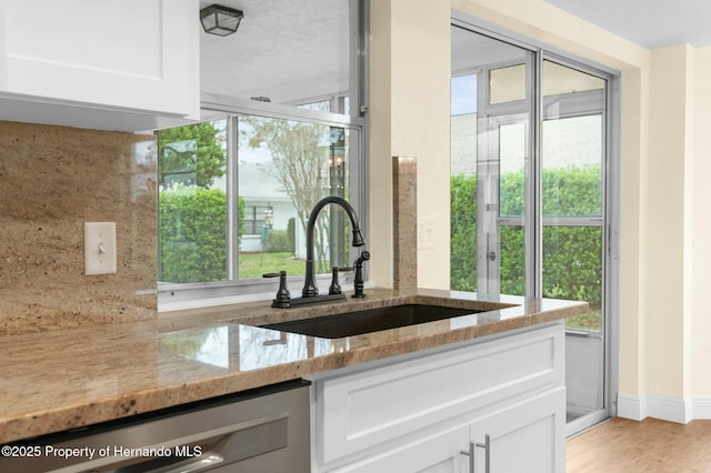 kitchen featuring dishwasher, light wood-style flooring, light stone countertops, white cabinetry, and a sink