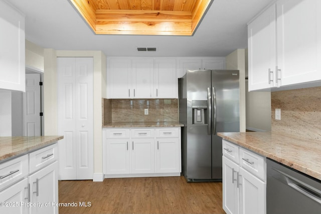 kitchen with a raised ceiling, visible vents, appliances with stainless steel finishes, white cabinetry, and light wood-type flooring