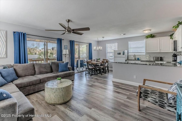 living room featuring ceiling fan with notable chandelier, light wood-style flooring, and baseboards