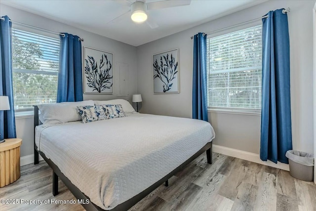 bedroom with a ceiling fan, multiple windows, baseboards, and wood finished floors