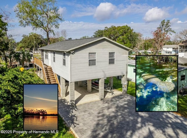 rear view of house featuring a shingled roof, a water view, stairway, a carport, and driveway