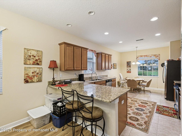 kitchen featuring visible vents, light stone counters, a peninsula, stainless steel appliances, and a sink