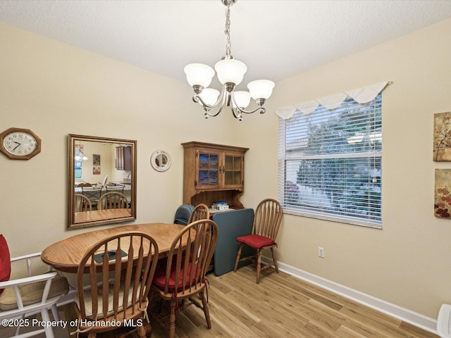 dining space with baseboards, light wood-style floors, and a notable chandelier