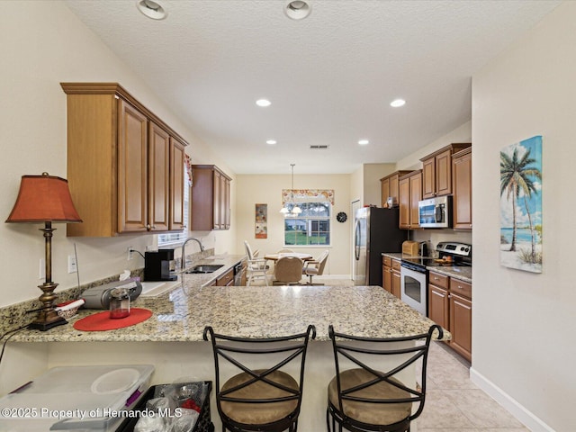 kitchen featuring brown cabinets, appliances with stainless steel finishes, a sink, a peninsula, and a kitchen bar