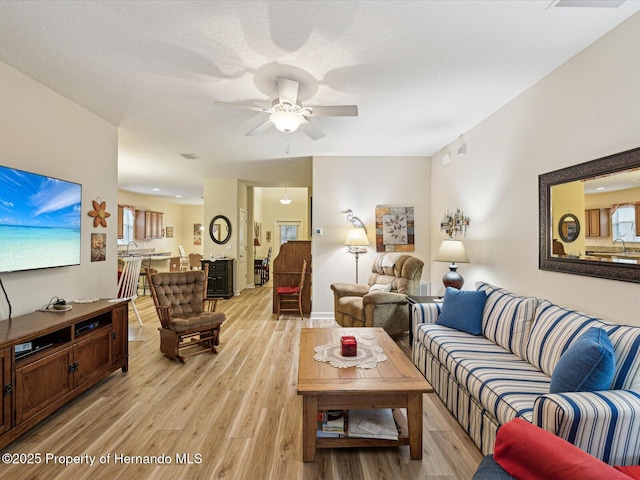 living room with light wood-type flooring, visible vents, and a ceiling fan