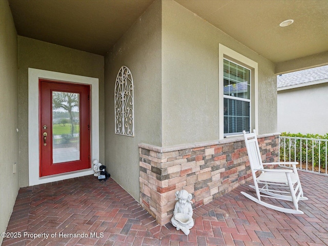 doorway to property featuring stone siding, covered porch, and stucco siding