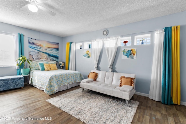 bedroom with a ceiling fan, a textured ceiling, baseboards, and wood finished floors