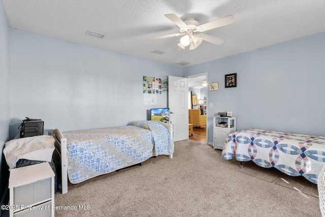 bedroom with a textured ceiling, visible vents, a ceiling fan, and light colored carpet