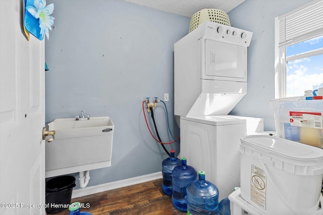 laundry area with a textured ceiling, laundry area, dark wood-style flooring, baseboards, and stacked washing maching and dryer