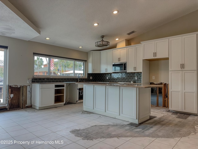 kitchen featuring stainless steel microwave, vaulted ceiling, visible vents, and white cabinetry