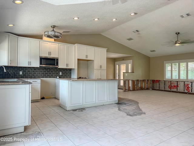 kitchen with lofted ceiling, stainless steel microwave, visible vents, a ceiling fan, and white cabinetry