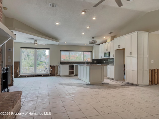 kitchen with ceiling fan, visible vents, white cabinets, a center island, and stainless steel microwave