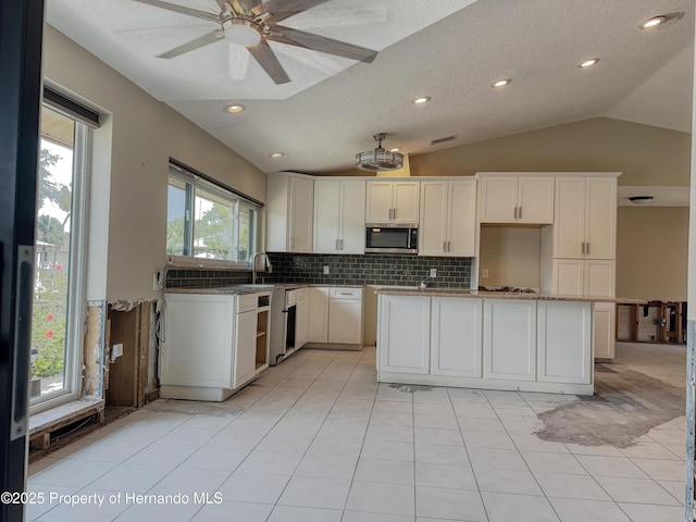 kitchen featuring lofted ceiling, a sink, white cabinetry, decorative backsplash, and stainless steel microwave