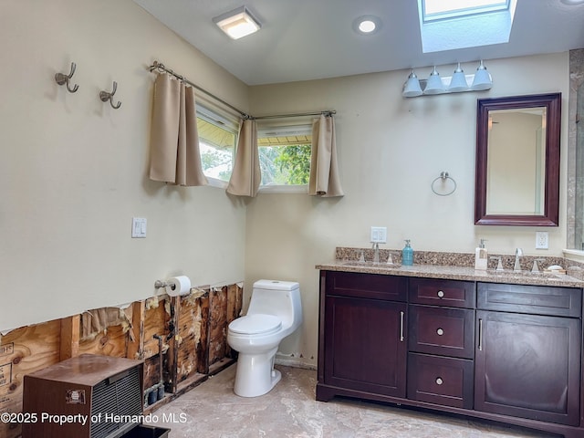 full bathroom featuring a skylight, a sink, toilet, and double vanity