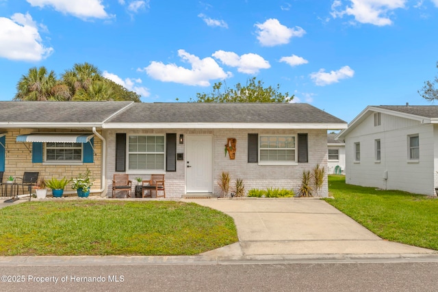 ranch-style home featuring a shingled roof, covered porch, brick siding, and a front lawn