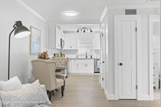 interior space with crown molding, visible vents, a sink, and light wood-style flooring