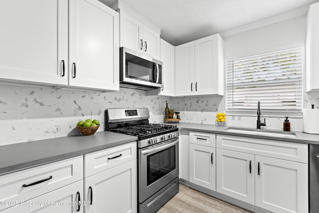 kitchen featuring appliances with stainless steel finishes, a textured ceiling, light wood-style floors, white cabinetry, and a sink