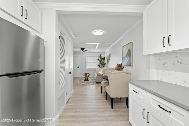 kitchen with crown molding, light countertops, freestanding refrigerator, white cabinetry, and light wood-type flooring