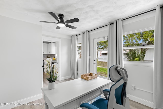 office space with light wood-style floors, ceiling fan, and baseboards