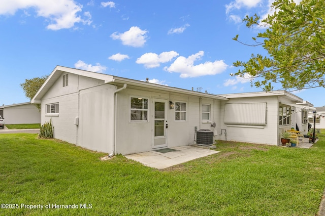 rear view of house featuring a yard, central AC unit, and concrete block siding