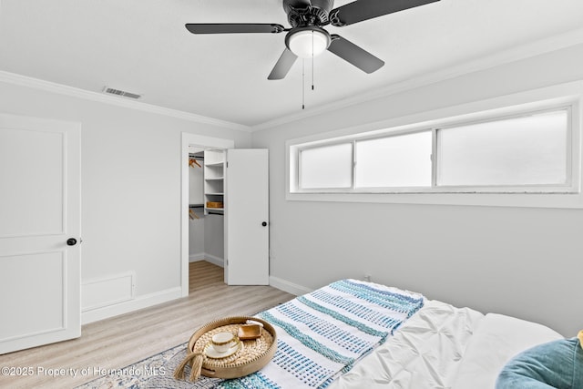 bedroom with crown molding, a spacious closet, light wood-style floors, ceiling fan, and baseboards