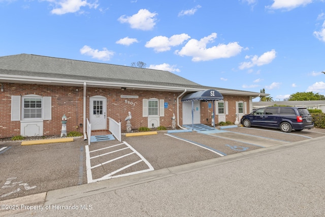 exterior space with a shingled roof, uncovered parking, and brick siding