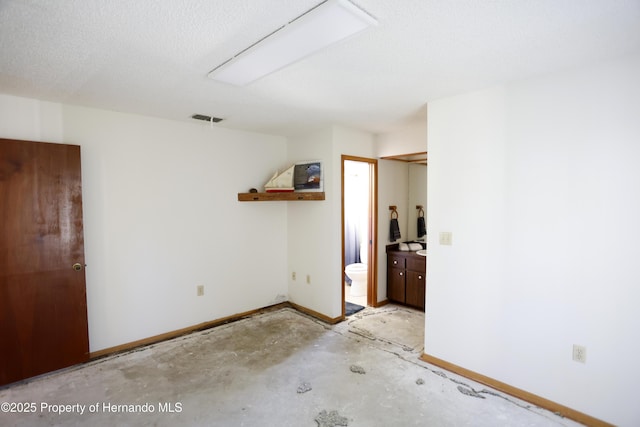 unfurnished bedroom featuring baseboards, visible vents, unfinished concrete flooring, ensuite bath, and a textured ceiling