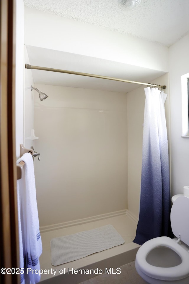 full bathroom featuring toilet, a stall shower, and a textured ceiling