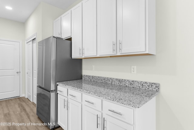 kitchen with recessed lighting, light wood-style floors, freestanding refrigerator, white cabinetry, and light stone countertops