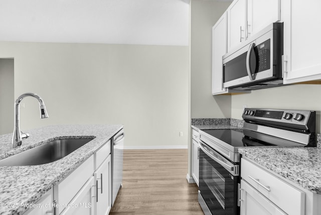 kitchen featuring white cabinets, light stone countertops, stainless steel appliances, and a sink