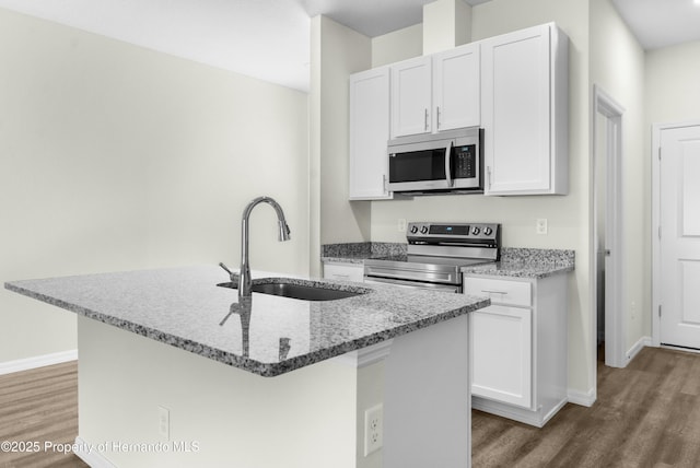 kitchen with stainless steel appliances, a kitchen island with sink, a sink, and white cabinetry