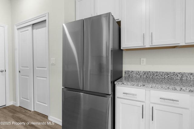 kitchen with light stone countertops, freestanding refrigerator, white cabinets, wood finished floors, and baseboards