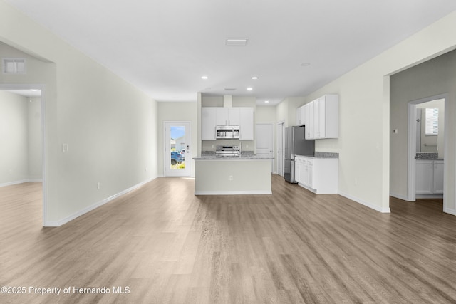 kitchen with visible vents, an island with sink, open floor plan, stainless steel appliances, and white cabinetry