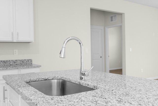 room details featuring light stone countertops, white cabinetry, visible vents, and a sink