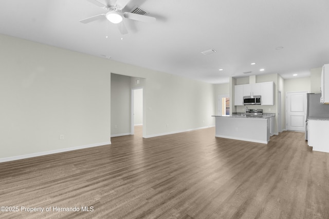 unfurnished living room with a ceiling fan, a sink, baseboards, and wood finished floors